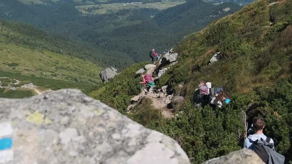 Group of Tourists and Children with Backpacks Go Down on Stone Trail in Mountain