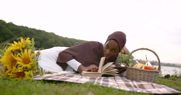 Black Woman in White Dress Reading at the River Bank
