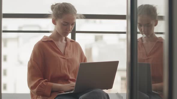 Woman Typing on Laptop Sitting by Window