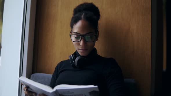 The Young Attractive Afroamerican Woman is Reading the Book on the Wide Windowsill