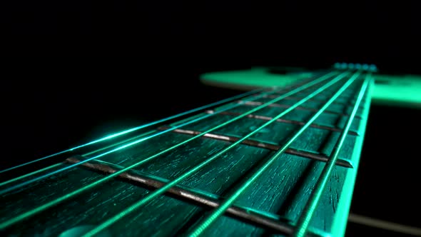 Camera Pans Over Fretboard of Classical Acoustic Guitar Against Black Background Illuminated By