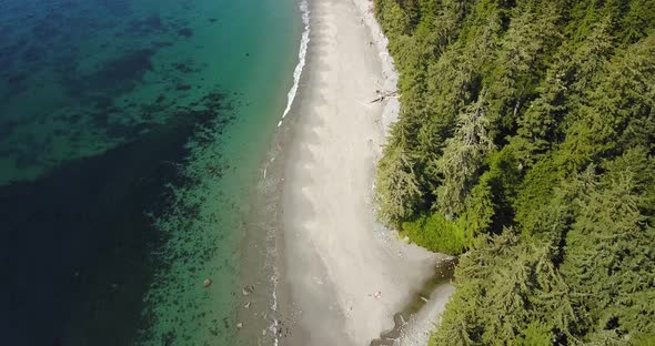 Aerial Daytime Wide Overhead Shot Flying Over A Creek Flowing Into Pacific Ocean Over Beach With Peo