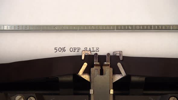 Typing phrase 50% OFF SALE on retro typewriter. Close up.