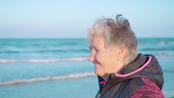 Old Woman with Hair Waved By Wind Enjoys Sea View on Coast