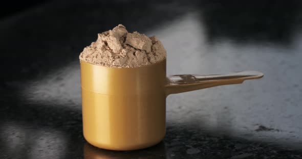 Whey Protein in a Measuring Spoon Closeup on a Dark Background with Movement