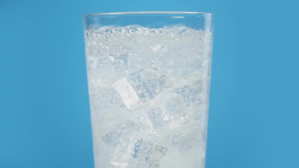 Glass Full of Cold Sparkling Water with Ice Cubes on Blue Background Transparent Fizzy Drink