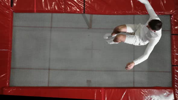 Top View Gymnast Acrobat in White Clothes Performs a Somersault on a Trampoline in Slow Motion