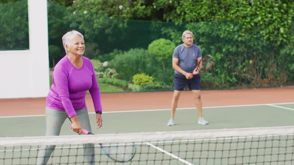 Video of happy biracial senior couple during training on tennis court