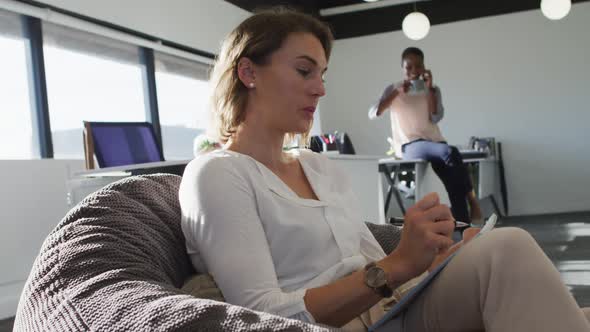 Caucasian businesswoman sitting in armchair, writing while her coworker having business call