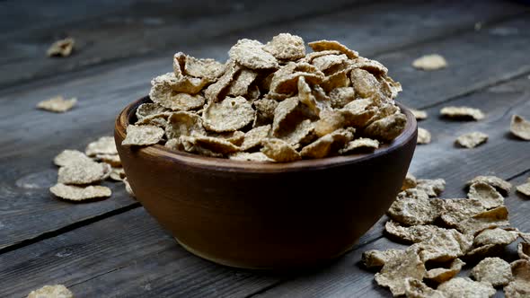 wheat flakes fall into a clay plate on a wooden table. A bowl of dry flakes