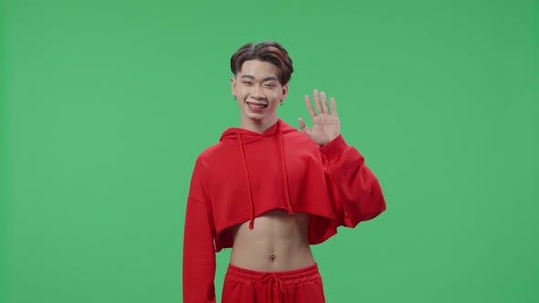 A Smiling Asian Transgender Male Waving Hand And Say Hi While Standing On Green Screen In The Studio