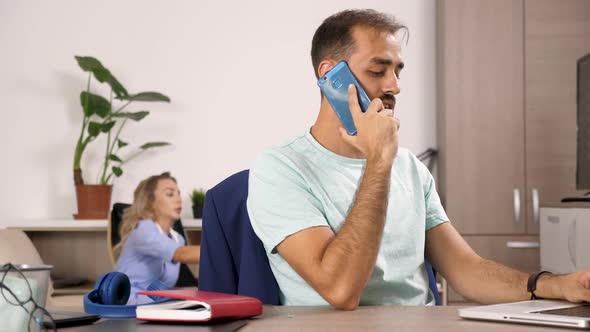 Man Talks on the Cellphone While a Woman Is Watching TV in the Background