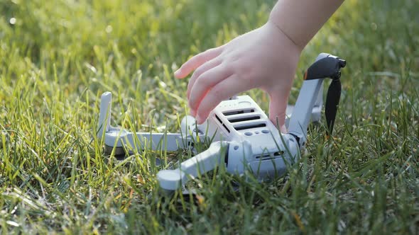 A Child's Hand Picks Up a Fallen Drone From a Green Lawn