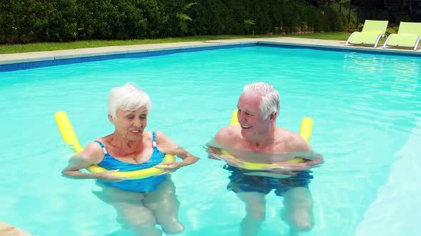 Senior couple swimming in the pool with inflatable tubes