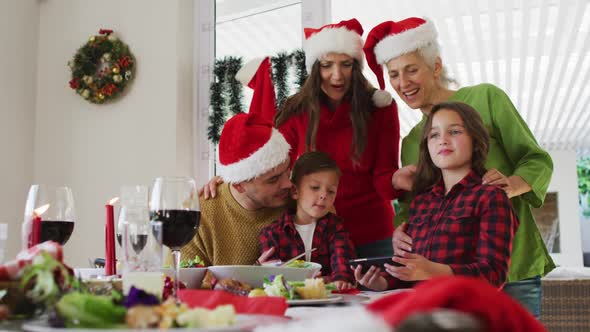 Happy caucasian multi generation family wearing santa hats looking at smartphone