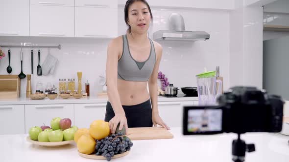 Blogger sporty Asian woman using camera recording how to make apple juice video for her subscriber.