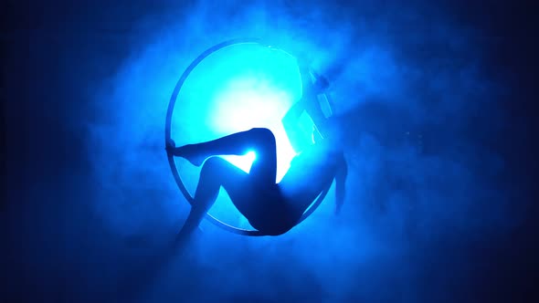 Silhouette Aerial Gymnast Performs Trick in Ring in Smoky Room with Backlit