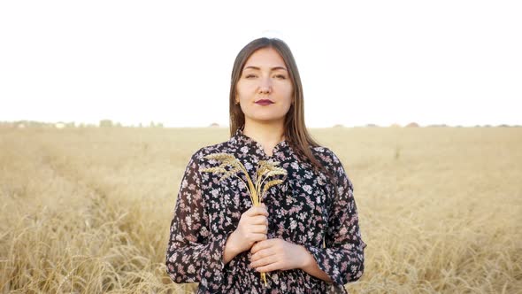 Portrait of a Brunette Woman with a Bouquet of Ears of Ripe Wheat in a Field