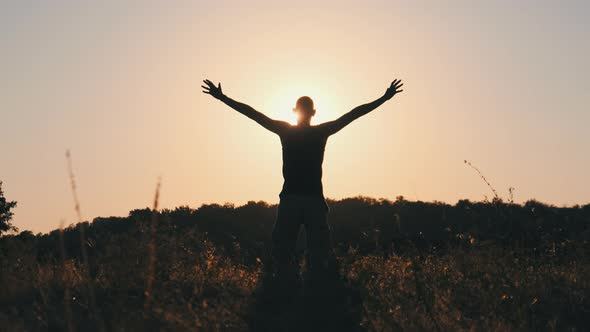 Silhouette of Young Man Against Sunset Raising Hands Sides and Up. Slow Motion