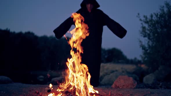 Fire flame on the dark background with black figure. Silhouette of death near the fire in the evenin