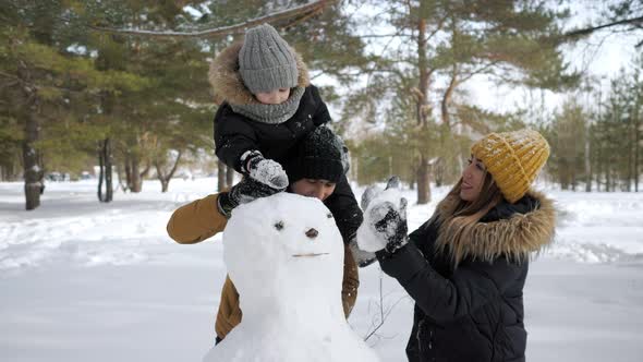 Young Family Mom Son and Dad are Building a Snowman in Winter City Park