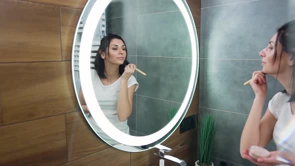 Brunette Which Standing in Front of Mirror and Using Brush to Put Powder on Her Face