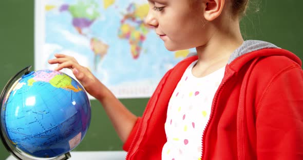 Schoolgirl looking at globe in classroom at school