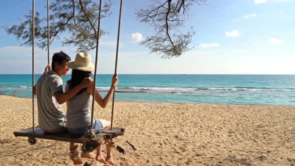 Happy Asian couple swinging on a swing at the beach during travel trip on holidays