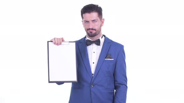 Stressed Young Bearded Businessman Showing Clipboard and Giving Thumbs Down