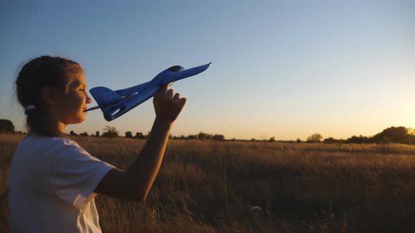 Carefree Small Girl Plays with Plane Going Along Grass Meadow at Sunset Time