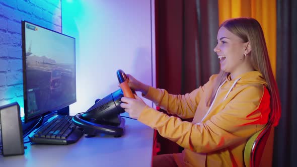 Girl playing a driving game. Girl sitting in room and holding the race steering wheel to play