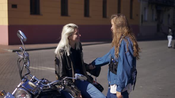 Two Young Women in Love and Mounted Motorcycle in the City Having Fun Together