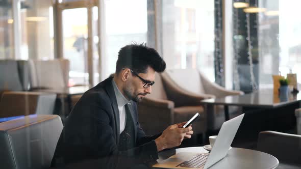 Confident Bearded Man in Glasses Using Smartphone During Coffee Break in Cafe