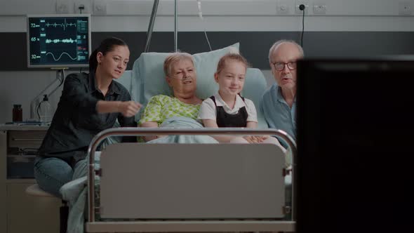 Visitors Watching Television with Elder Patient in Hospital Ward