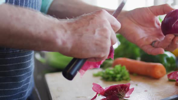 Closeup of mans hands cutting red onion on a cutting board