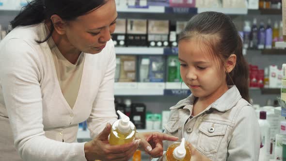 A Girl with Her Daughter Chooses Tubes of Cosmetic in a Pharmacy