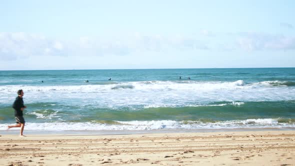 Surfers paddle out to catch waves as a man jogs on the shore of the beach.