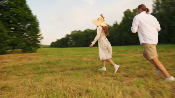 A Man Photographs a Woman in a Straw Hat on a Film Camera in a Field at Sunset