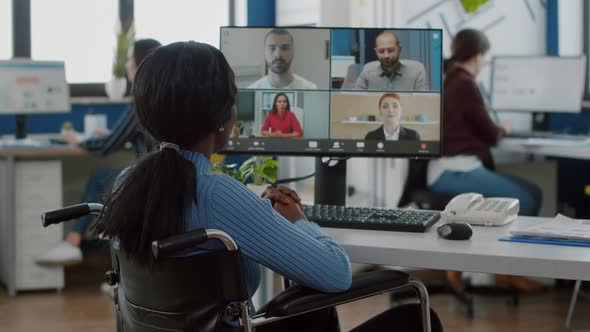 Paralyzed Black Worker Sitting Immobilized in Wheelchair Having Videomeeting