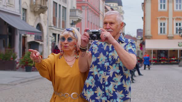 Elderly Stylish Tourists Man and Woman Taking Photos with Old Film Camera Walking Along City Street