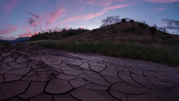 Sunset time lapse over dry cracked mud with pink clouds