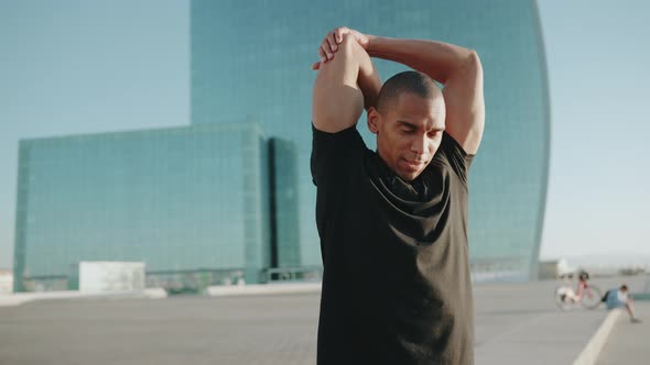 Strong bald sportsman wearing black t-shirt doing exercise outdoors