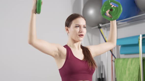 a Beautiful and Slender Young Woman Does Exercises with Weights in the Gym