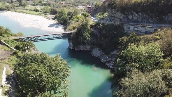 River with blue water. Bridge over river. On the shore are small stones. The shore is rocky. Aerial