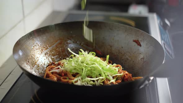 a Female Chef's Hand Throws Chinese Cabbage Onto a Hot Wok with Noodles