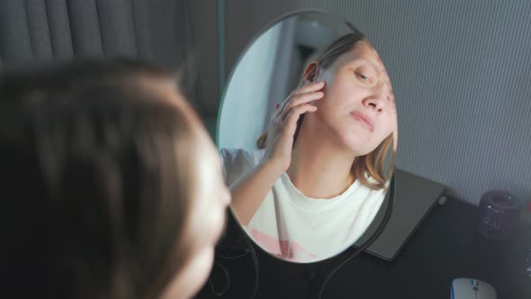 Young Woman Looks at Herself in the Mirror Examines the Skin of Her Face and Gets Upset