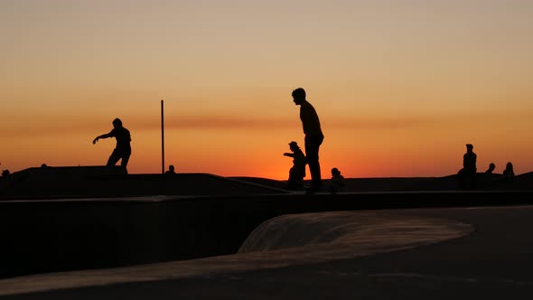 Silhouette of Young Jumping Skateboarder Riding Longboard, Summer Sunset Background. Venice Ocean