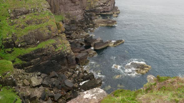 Looking up from a rocky bay and out into the vast Atlantic ocean as waves gently lap against a tall