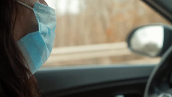 Girl with Medical Mask To Protect Her From Virus Driving a Car. Coronavirus Concept.