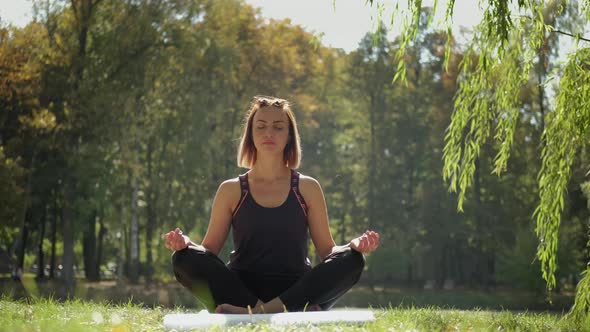 Woman Sitting on Yoga Mat and Practicing Yoga Exercise Outdoors in Sunny Day